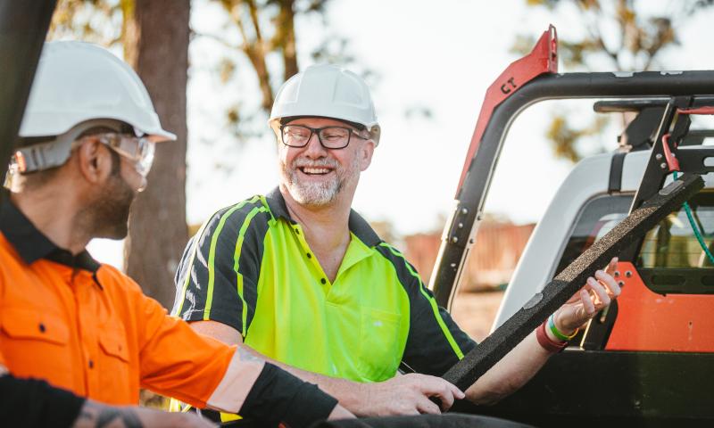 Two construction workers in high-vis clothing smiling at each other
